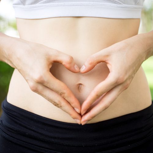 Close-up of female hands shaping heart on belly outdoors. Fitness and dieting concept