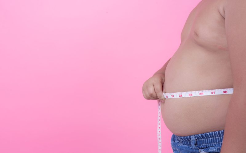 Obese boy who is overweight on a pink background.